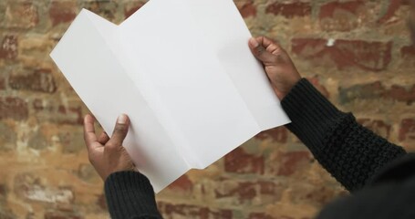 Wall Mural - Video of hand of african american man holding white blank page, copy space over brick wall