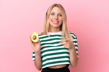 Wall Mural - Young caucasian woman holding an avocado isolated on pink background surprised and pointing front