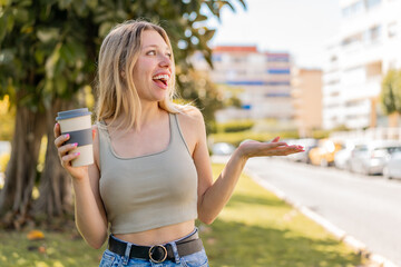 Wall Mural - Young blonde woman holding a take away coffee at outdoors with surprise facial expression