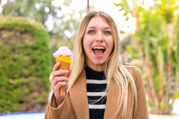 Wall Mural - Young pretty blonde woman with a cornet ice cream at outdoors with surprise and shocked facial expression