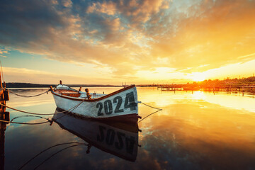 Wall Mural - 2024 concept Fishing Boat on Varna lake with a reflection in the water at sunset.