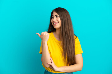 Wall Mural - Young caucasian woman isolated on blue background pointing to the side to present a product