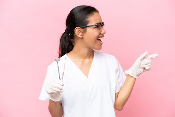 Wall Mural - Dentist Colombian woman isolated on pink background pointing finger to the side and presenting a product