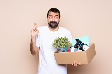 Wall Mural - Man holding a box and moving in new home over isolated background with fingers crossing and wishing the best