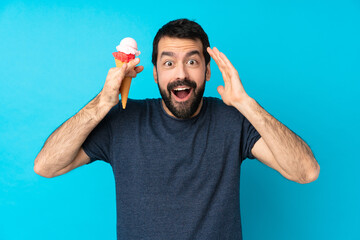 Wall Mural - Young man with a cornet ice cream over isolated blue background with surprise expression