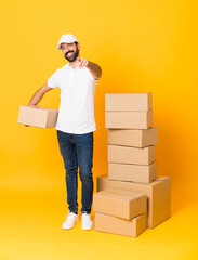 Wall Mural - Full-length shot of delivery man among boxes over isolated yellow background points finger at you with a confident expression