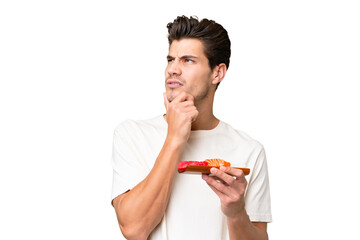 Wall Mural - Young caucasian man holding sashimi over isolated background having doubts