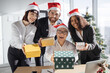 © sofiko14 - Multiethnic team of people giving presents during christmas festivity, celebrating winter holiday in startup office. Coworkers exchanging xmas gifts, seasonal festive decorations.