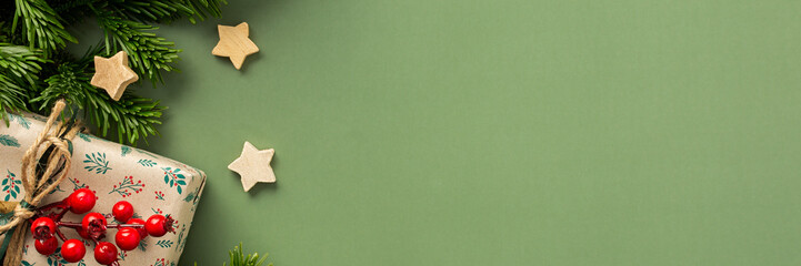 Wall Mural - Christmas festive banner, fir branches and gift boxes with a sprig of rowan and wooden stars on a green background, top view