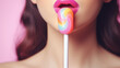 Close-up of brightly colored female lips eating and licking a candy lollipop on a stick isolated on flat background with copy space.