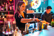 © ADDICTIVE STOCK - Focused young Barkeeper with blonde hair standing at counter while preparing drink at bar
