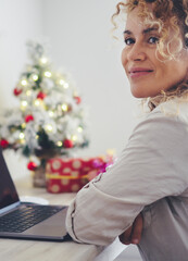 Wall Mural - Side portrait view of attractive young adult woman smiling and thinking with laptop in front and christmas decorations in background. Happy female people enjoy xmas holiday leisure activity at home