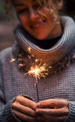 Wall Mural - Front view of happy woman celebrating with sparkler light in outdoor. Foreground focus on fire and female people smiling in background. New year eve and anniversary or birthday celebration alone