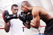 Black man, boxer and personal trainer in ring fight at gym for workout, exercise or self defense training together. African male person with boxing or sparing partner preparing for sports competition