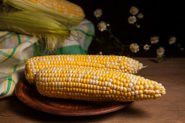 Clay plate with two cobs sweet corn on wooden background..