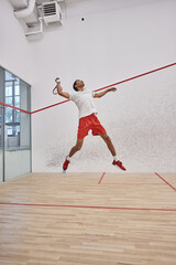 Wall Mural - motion shot, energetic african american player holding racquet while jumping and playing squash