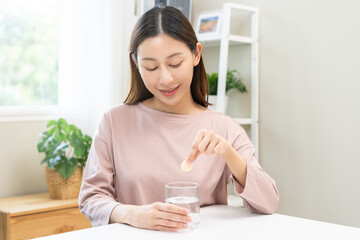 Smile asian young woman putting or dropping effervescent tablet into glass of water, holding pain pill, painkiller medicine, aspirin for treatment, take vitamin c for hangover. Health care concept.