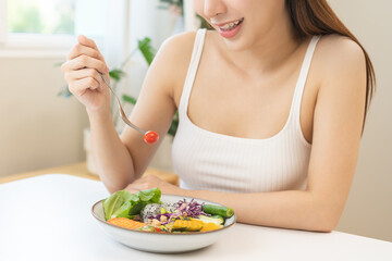 Wall Mural - Diet concept, happy asian young woman hand use a fork to prick tomato, fresh vegetable or green salad, eat nutrition food  on table at home, low fat to good body. Girl getting weight loss for healthy.