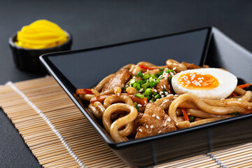 Wall Mural - Udon noodles with meat, egg, onion, carrot and chili pepper on a dark background.