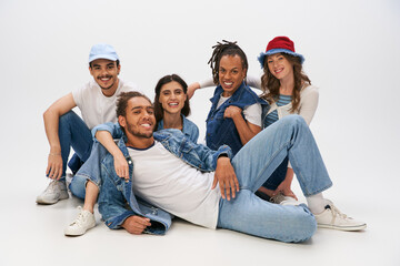 Wall Mural - cheerful african man in denim wear lying down near interracial friends looking at camera on grey