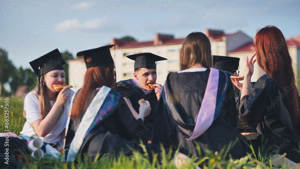 Graduates in black suits eating pizza in a city meadow. Stock Photo ...