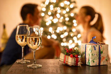 Wall Mural - Young couple enjoying a romantic Christmas Eve with focus on wine gifts next to the Christmas tree 