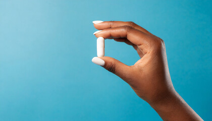 female hand holding white capsule on blue background close copy space pharmacology concept