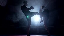 Two fighters battling each other inside boxing ring with dramatic backlight. Opponents kicking and punching each other in intense fight training