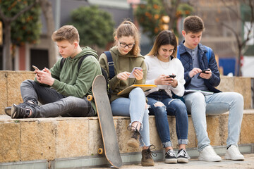 Teenage schoolers boys and girls using their gadgets outside on sunny day