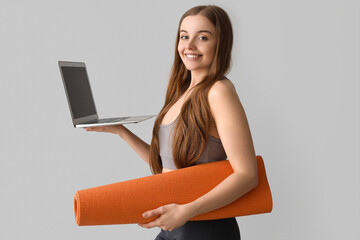 Wall Mural - Sporty young woman with yoga mat and laptop on grey background