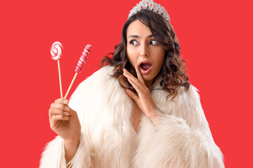 Wall Mural - Shocked young woman in tiara with lollipops on red background