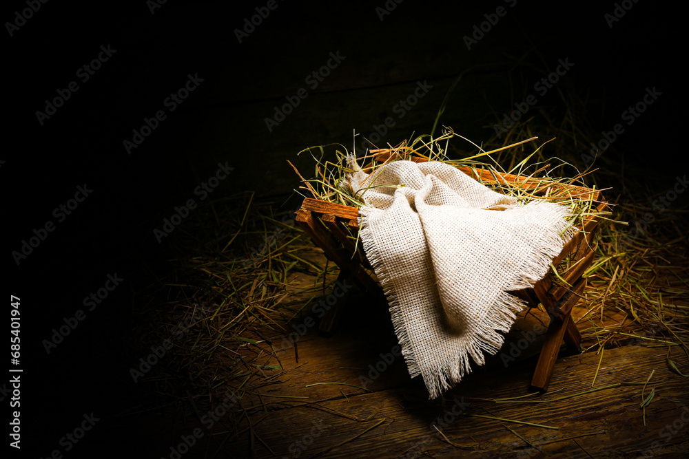 Manger with cloth and hay on wooden table against dark background