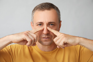 Poster - Ill mature man pointing at nose on grey background