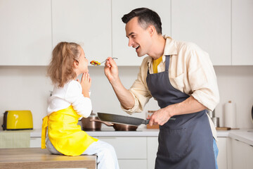 Wall Mural - Happy father feeding his little daughter in kitchen