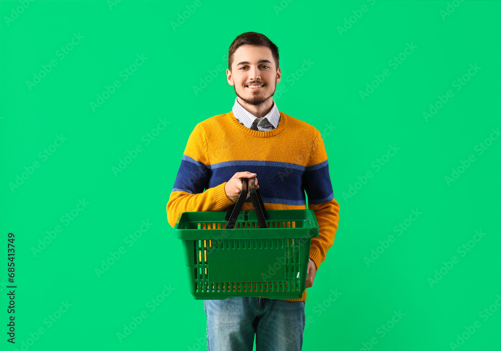 Young man with shopping basket on green background