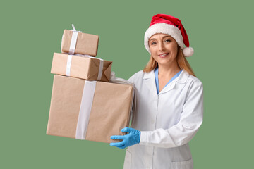 Poster - Mature female doctor in Santa hat with Christmas gift boxes on green background