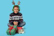 © Pixel-Shot - Little African-American boy in winter clothes with deer horns and gifts on blue background