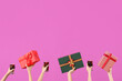 Female hands with glasses of warm mulled wine and gift boxes on pink background