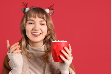 Poster - Pretty young woman holding cup of hot chocolate with marshmallows on red background