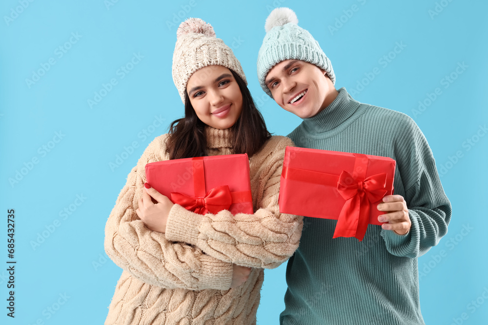 Happy young couple with Christmas presents on blue background
