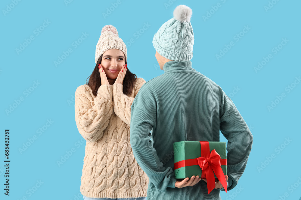 Young man giving his girlfriend Christmas gift on blue background
