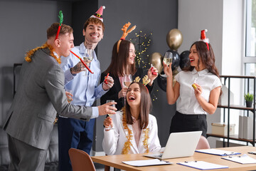 Wall Mural - Young colleagues with party blowers and champagne celebrating New Year in office