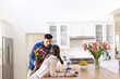 Happy diverse couple holding flowers and looking at each other in kitchen at home, copy space