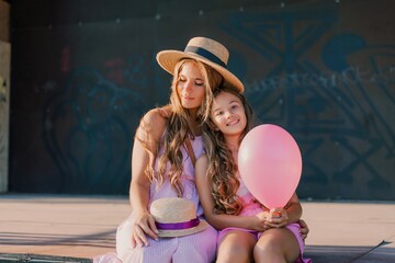 Wall Mural - Portrait of mother and daughter in pink dresses with flowing long hair against the black backdrop. The woman hugs and presses the girl to her.