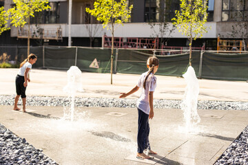 Wall Mural - Happy teenage girl dancing in a fountain in a city park on a hot summer day.