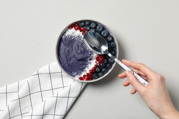 Wall Mural - Bowl with smoothies, towel and spoon in hand on gray background, top view