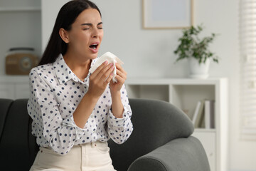 Poster - Suffering from allergy. Young woman with tissue sneezing at home, space for text