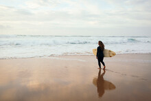 Woman With Surfboard Walking Towards Sea At Beach