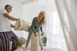 © Westend61 - Man pillow fighting with woman on bed at home