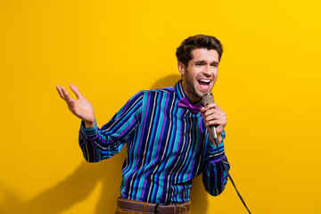 Poster - Photo of handsome man dressed striped shirt bow tie sing song hold microphone look empty space isolated on yellow color background